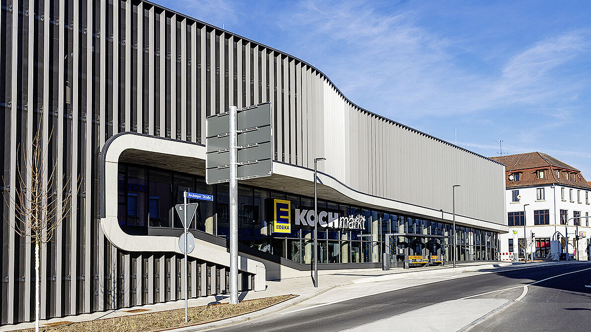 Nouvelle construction Edeka : une façade 3D impressionnante et partiellement transparente en tôles perforées. Les surfaces sont revêtues par poudre en fer micacé mat.